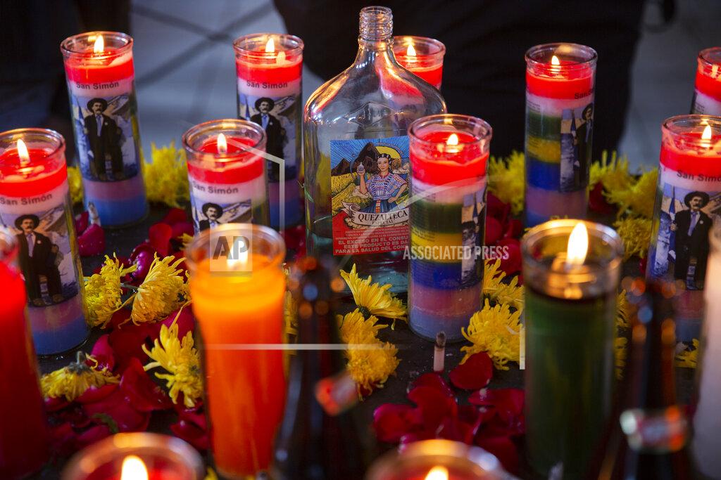 Moises Castillo A bottle of liquor is surrounded by burning candles with images of folk saint Maximon, an Indigenous character worshipped mainly by Indigenous people, inside a temple known as Maximon church on his feast day in San Andres Itzapa, Guatemala, Wednesday, Oct. 28, 2020. To help curb the spread of the new coronavirus, the annual celebration was limited to local residents who waited in line to enter the church little by little, and it was closed to pilgrims who normally travel here from across the country. (AP Photo/Moises Castillo)