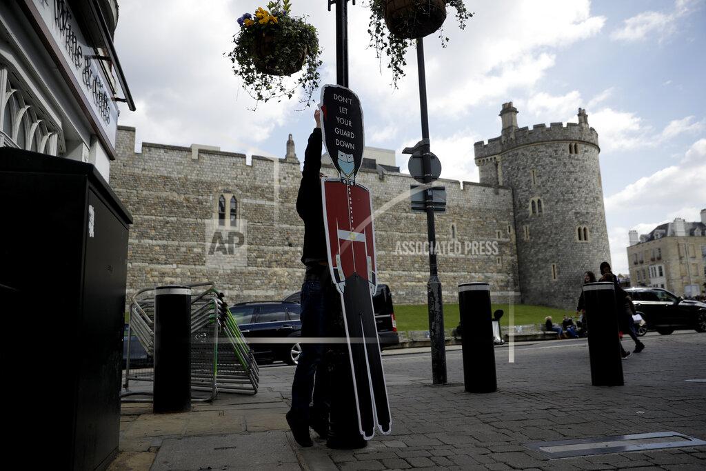Matt Dunham A worker puts up a cutout of a guardsman with a message reminding people not to let their guard down with regards to coronavirus, to coincide with non-essential shops being reopened this week, outside Windsor Castle, in Windsor, England, Wednesday, April 14, 2021. Britain's Prince Philip, husband of Queen Elizabeth II, died Friday April 9 aged 99. His funeral service will take place on Saturday at Windsor Castle. (AP Photo/Matt Dunham)