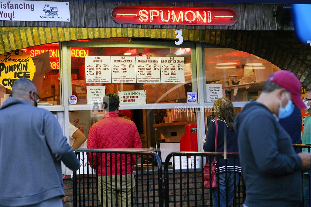 Kathy Willens People place orders at L&B Spumoni Gardens, Sunday, Oct. 4, 2020, in the Bensonhurst/Gravesend section of the Brooklyn borough of New York. The popular neighborhood pizzeria that is also famous for its Italian ices may be forced to close down its outdoor dining area after New York's mayor said Sunday that he has asked the state for permission to close schools and reinstate restrictions on nonessential businesses in several neighborhoods because of a resurgence of the coronavirus. (AP Photo/Kathy Willens)