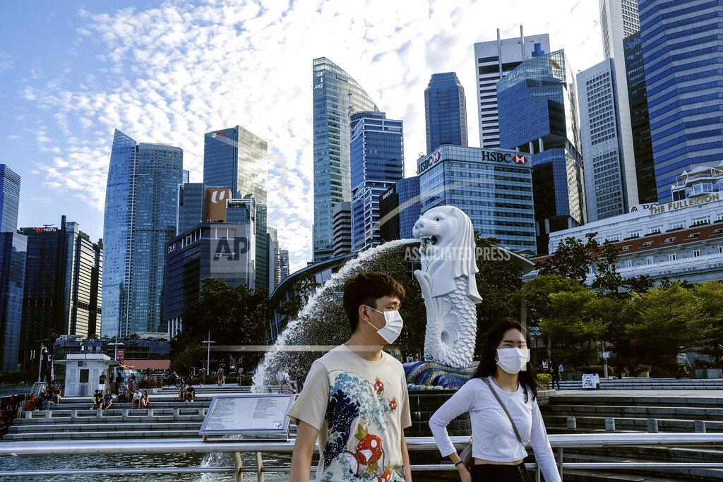 Ee Ming Toh FILE - In this March 14, 2020, photo, a couple wearing face masks walk past the Merlion statue in Singapore. A second wave of coronavirus infections in tightly packed foreign workers' dormitories has caught Singapore off guard, and exposed the danger of overlooking marginal groups in a health crisis. Infections in Singapore, an affluent Southeast Asian city-state of fewer than 6 million people, have jumped more than a hundredfold in two months — from 226 in mid-March to over 23,000, the most in Asia after China and India. (AP Photo/Ee Ming Toh, File)