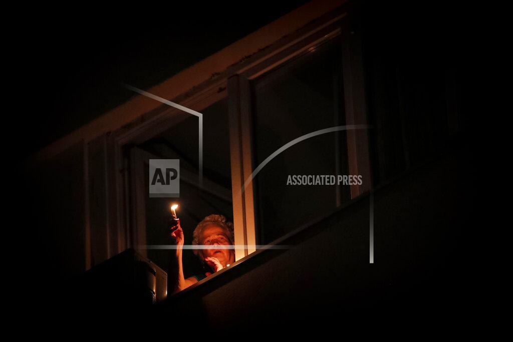 Vadim Ghirda A woman holds a candle at the window while listening to the blessings of a priest from downstairs during the coronavirus pandemic in Bucharest, Romania, Saturday, April 18, 2020. Priests accompanied by volunteers distributed the holy light ahead of the usual time, at midnight, as people observed the interdiction to join religious celebrations in the week leading to the Orthodox Easter, imposed across Romania as authorities try to limit the spread of the COVID-19 infections. (AP Photo/Vadim Ghirda)