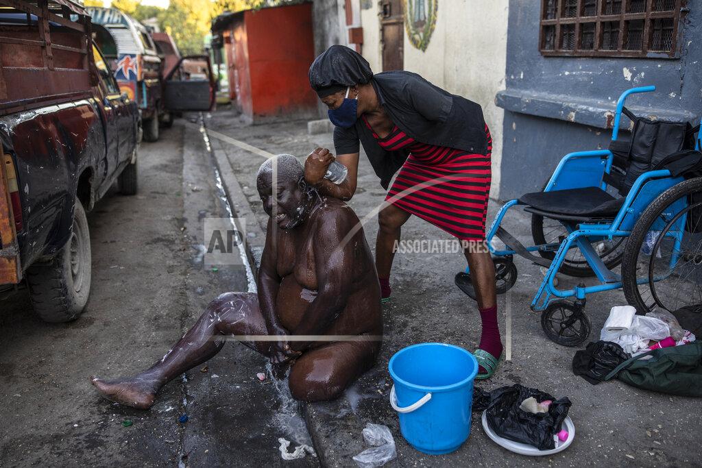 Rodrigo Abd Marie Joseph bathes her friend Jean Robert outside a shelter for the internally displaced where they live due to police violence in Port-au-Prince, Haiti, Thursday, Sept. 16, 2021. Most of the population of Port-au-Prince has no access to basic public services, no drinking water, electricity or garbage collection. (AP Photo/Rodrigo Abd)