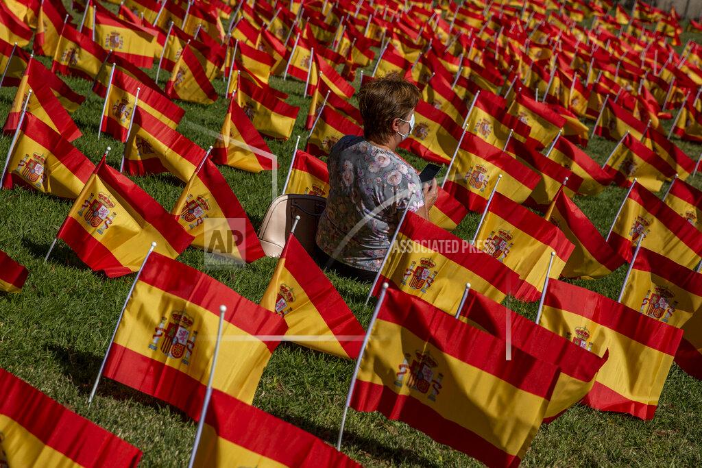 Manu Fernandez A woman sits among the Spanish flags placed in memory of coronavirus (COVID-19) victims in Madrid, Spain, Sunday, Sept. 27, 2020. An association of families of coronavirus victims has planted what it says are 53,000 small Spanish flags in a Madrid park to honor the dead of the pandemic. (AP Photo/Manu Fernandez)