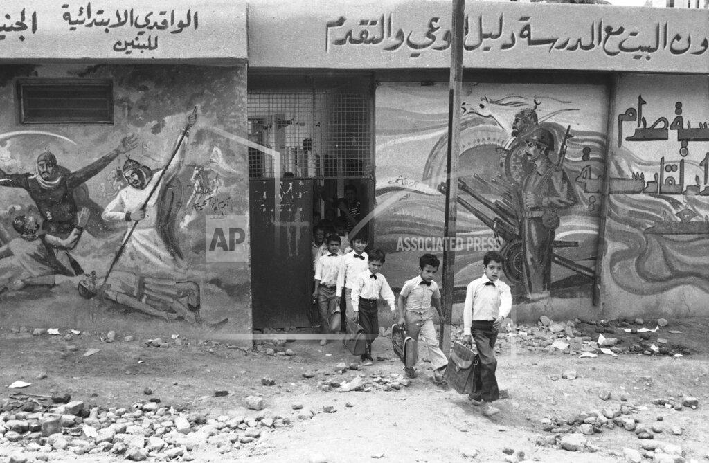 Herve Merliac FILE - In this April 28, 1984 file photo, elementary school pupils, dressed in the standard white shirt school uniform of Iraq, leave their school in Baghdad. Scenes on the wall depict the Iraq-Iran war as a new battle between Arabia and Persia. The Iran-Iraq war launched by Iraq's Saddam Hussein after the Iranian revolution resulted in around half a million deaths. A generation was decimated in both countries. (AP Photo/Herve Merliac)