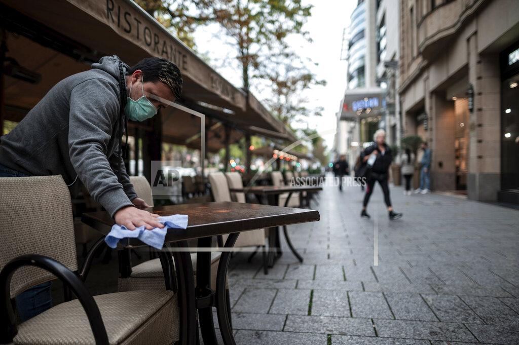 Fabian Strauch An employee wearing a mouth and nose protector wipes tables in a restaurant on the shopping street Koenigsallee in Duesseldorf, Germany, Friday, Oct. 9, 2020. The corona pandemic is increasingly becoming a problem in the large cities and conurbations of North Rhine-Westphalia. (Fabian Strauch/dpa via AP)
