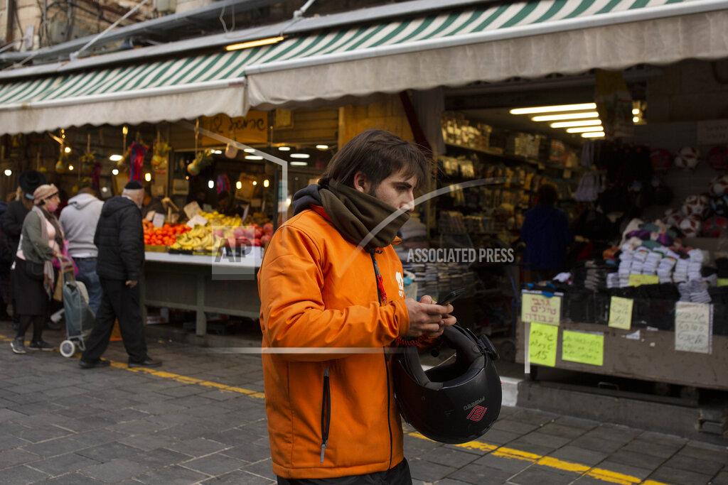 Maya Alleruzzo A dood delivery driver carries his smart phone in the Mahane Yehuda market in Jerusalem, Wednesday, Dec. 23, 2020. In the early days of the pandemic, a panicked Israel began using a mass surveillance tool on its own people, tracking civilians’ mobile phones to halt the spread of the coronavirus. But months later, the tool’s effectiveness is being called into question and critics say its use has come at an immeasurable cost to the country’s democratic principles. (AP Photo/Maya Alleruzzo)