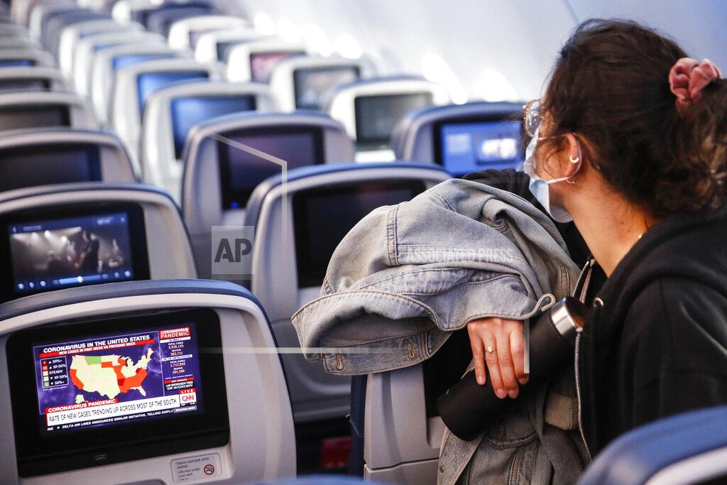 A passenger wears personal protective equipment on a Delta Airlines flight as a map depicting the spread of COVID-19 is displayed on a monitor after landing at Minneapolis−Saint Paul International Airport, Thursday, May 28, 2020, in Minneapolis. (AP Photo/John Minchillo)