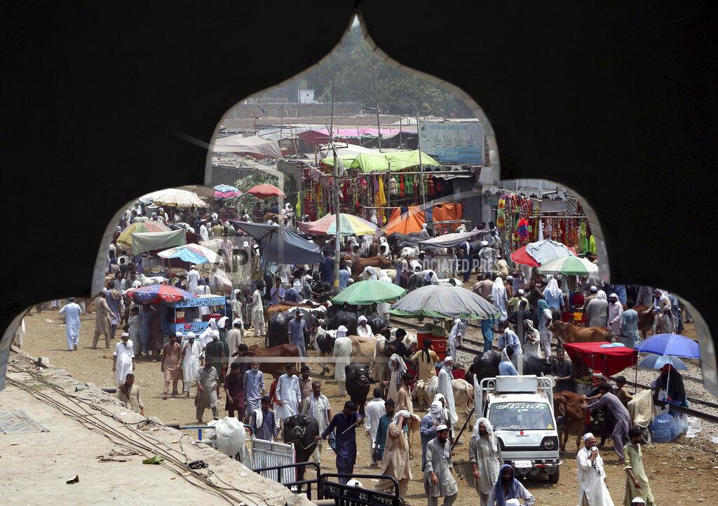 Muhammad Sajjad People visiting a cattle market to buy animals for the upcoming Muslim Eid al-Adha, or Feast of Sacrifice holiday, are seen through an arch of a nearby building, in Peshawar, Pakistan, Sunday, July 18, 2021. Eid al-Adha, the most important Islamic holiday, marks the willingness of the Prophet Ibrahim, Abraham to Christians and Jews, to sacrifice his son. (AP Photo/Muhammad Sajjad)