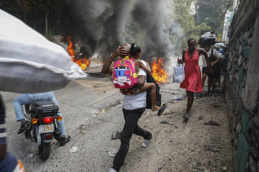 People walk past burning tires during a protest against Haitian Prime Minister Ariel Henry in Port-au-Prince, Haiti, Monday, Feb. 5, 2024. Banks, schools and government agencies closed in Haiti&rsquo;s northern and southern regions on Monday while protesters blocked main routes with blazing tires and paralyzed public transportation, according to local media reports. (AP Photo/Odelyn Joseph)