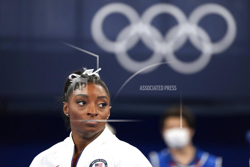 Simone Biles, of the United States, watches gymnasts perform after she exited the team final with apparent injury, at the 2020 Summer Olympics, Tuesday, July 27, 2021, in Tokyo. The 24-year-old reigning Olympic gymnastics champion Biles huddled with a trainer after landing her vault. She then exited the competition floor with the team doctor. (AP Photo/Ashley Landis)