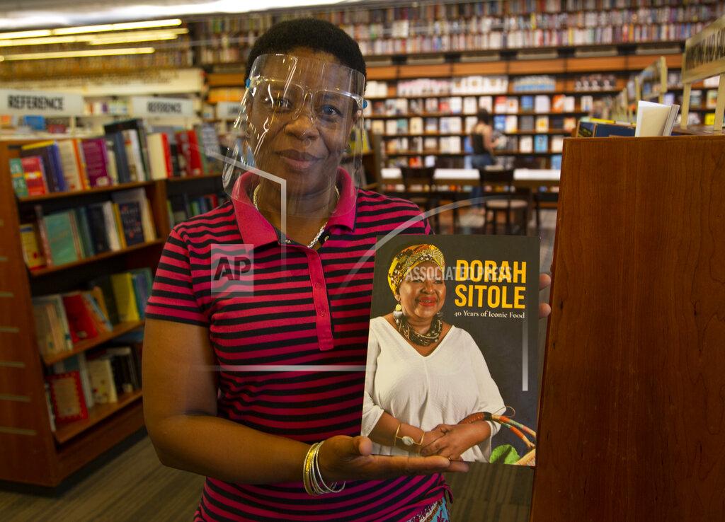 Denis Farrell Book store worker, Dikeledi Nhlapo, holds a copy of Dorah Sitole's "40 Years of Iconic Food" cook book in Exclusive Books in Hyde Park Corner, Johannesburg, Tuesday, Jan. 12, 2021. South Africa's pioneer Black food writer Sitole, portrait on cover, who quietly defied apartheid to win respect and a wide readership for African cuisine, died January 2021, of COVID-19. (AP Photo/Denis Farrell)