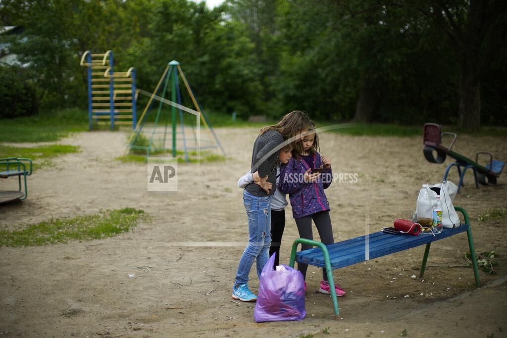 Francisco Seco Sisters Valeria, Sonya and Alina, from left, watch a music video in a cell phone in a children's playground near their home in Bakhmut, eastern Ukraine, Tuesday, May 24, 2022. The town of Bakhmut has been coming under increasing artillery strikes, particularly over the last week, as Russian forces try to press forward to encircle the city of Sieverodonetsk to the northeast. (AP Photo/Francisco Seco)