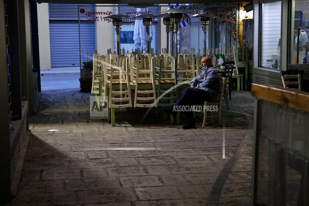 Petros Karadjias A man wearing a face mask sits by stacked chairs outside of a closed restaurant in central Nicosia, Cyprus, Thursday, Feb. 25, 2021. Cyprus will send all high school students back to their classrooms and open up gyms, pools, dance academies and art galleries next week in a further, incremental easing of the country's second nationwide COVID-19 lockdown. (AP Photo/Petros Karadjias)