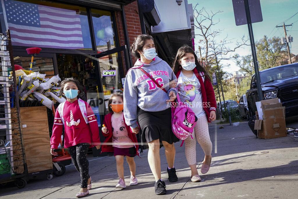John Minchillo Pedestrians in masks pass a store on Thursday, Oct. 15, 2020, as government restrictions on business activity limit operations due to an increase of COVID-19 cases, in the Far Rockaway neighborhood of the borough of Queens in New York. After shutdowns swept entire nations during the first surge of the coronavirus earlier this year, some countries and U.S. states are trying more targeted measures as cases rise again around the world. (AP Photo/John Minchillo)