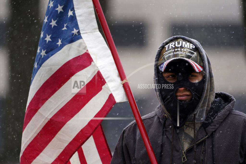 Paul Sancya A man stands outside the state capitol wearing a Trump hat with an American flag in Lansing, Mich., Sunday, Jan. 17, 2021. (AP Photo/Paul Sancya)