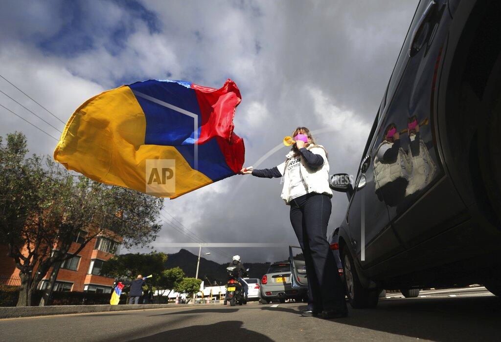 A supporter of former President Alvaro Uribe waving a national flag takes part in a caravan to protest the Supreme Court decision to place Uribe under house arrest while it advances a witness tampering investigation against him, in Bogota, Colombia, Friday, Aug. 7, 2020. (AP Photo/Fernando Vergara)