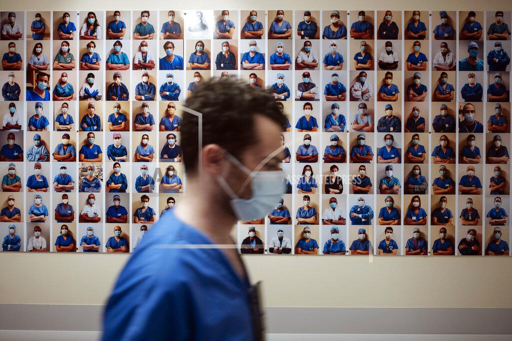 A member of staff passes in front of a collection of portraits of medical staff at Bichat Hospital, AP-HP, in Paris, Thursday, April 22, 2021. France still had nearly 6,000 critically ill patients in ICUs this week as the government embarked on the perilous process of gingerly easing the country out of its latest lockdown, too prematurely for those on pandemic frontlines in hospitals. President Emmanuel Macron's decision to reopen elementary schools on Monday and allow people to move about more freely again in May, even though ICU numbers have remained stubbornly higher than at any point since the pandemic's catastrophic first wave, marks another shift in multiple European capitals away from prioritizing hospitals. (AP Photo/Lewis Joly)