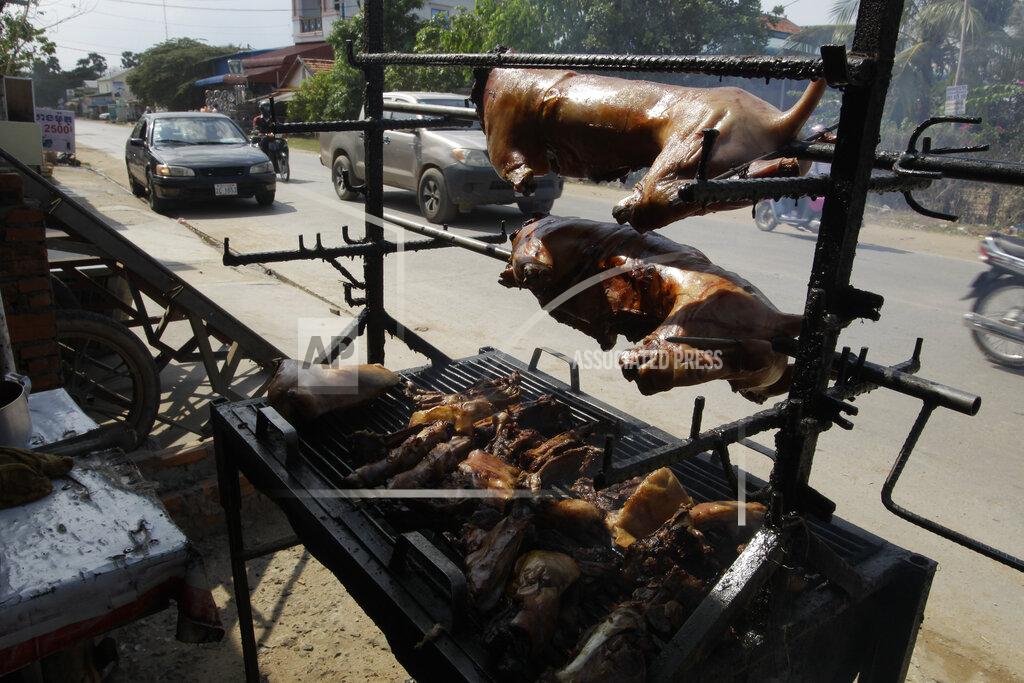 FILE - In this Mar. 30, 2017, file photo, a local vendor grills dog meat on the sidewalk on the outskirts of Phnom Penh, Cambodia. Early this week on Monday, July 6, 2020 in Siem Reap, home of the famous Angkor Wat temple complex, the local government issued a ban on the buying, selling and butchering of dogs for food. (AP Photo/Heng Sinith, File)