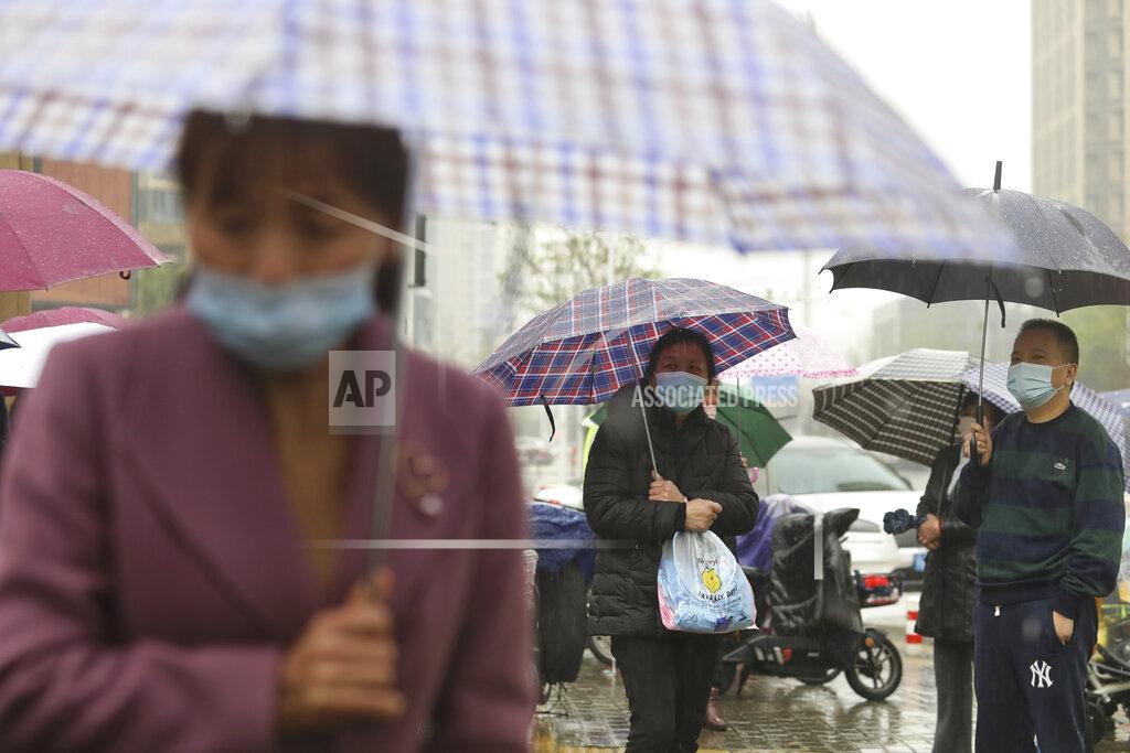 Uncredited People wearing face masks to protect against COVID-19 wait in the rain to pick up children from a school in Wuhan in central China's Hubei Province, Friday, March 26, 2021. Chinese officials briefed diplomats Friday on the ongoing research into the origin of COVID-19, ahead of the expected release of a long-awaited report from the World Health Organization. (Chinatopix via AP)