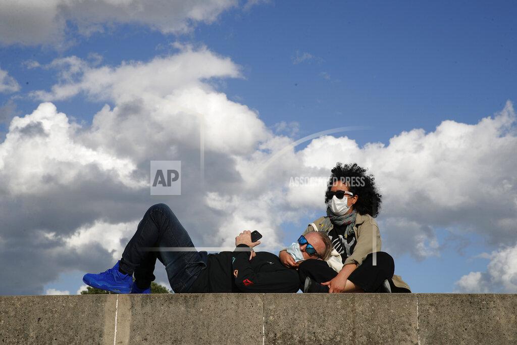 Francois Mori Parisians, wearing protective masks, sit in the sun along the closed Tuileries garden in Paris, Saturday, May 23, 2020 as France gradually lifts its COVID-19 lockdown. (AP Photo/Francois Mori)