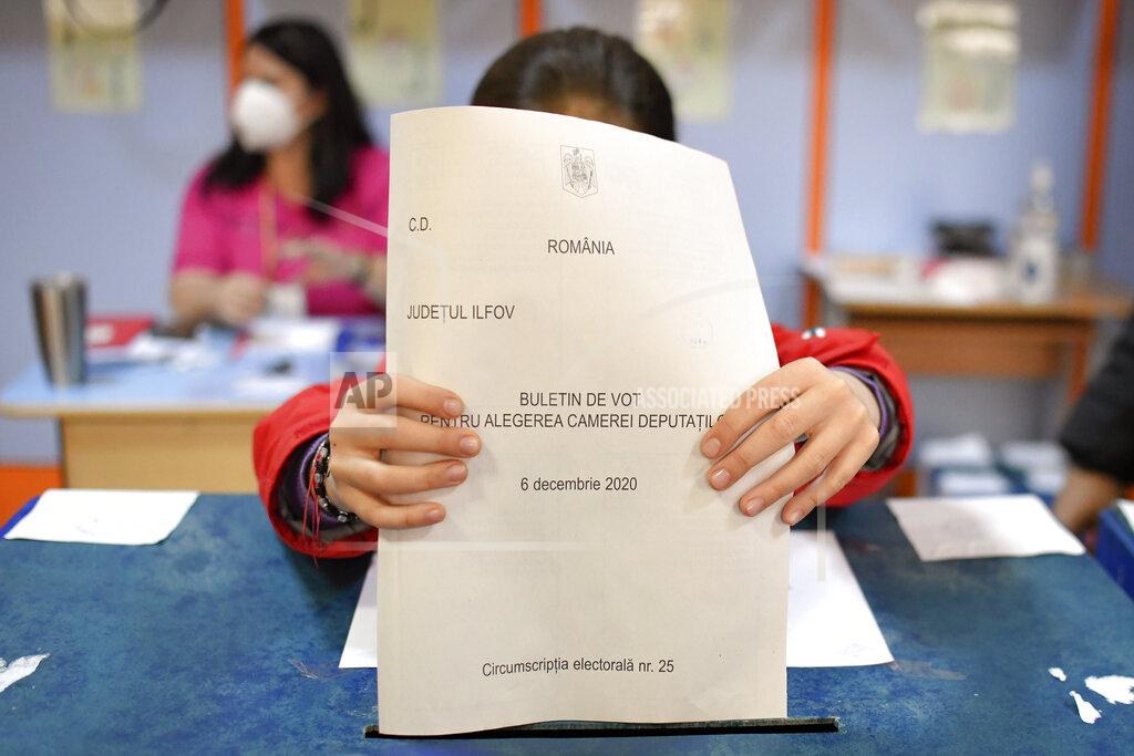 Andreea Alexandru A child wearing a mask for protection against the COVID-19 infection places and adult's vote into the ballot box in the village of Branesti, Romania, Sunday, Dec. 6, 2020. Voting started in Romania's legislative election expected to restore some measure of stability after five years of political and social turbulence with more than 18 million Romanians registered to vote for a new legislative body. (AP Photo/Andreea Alexandru)