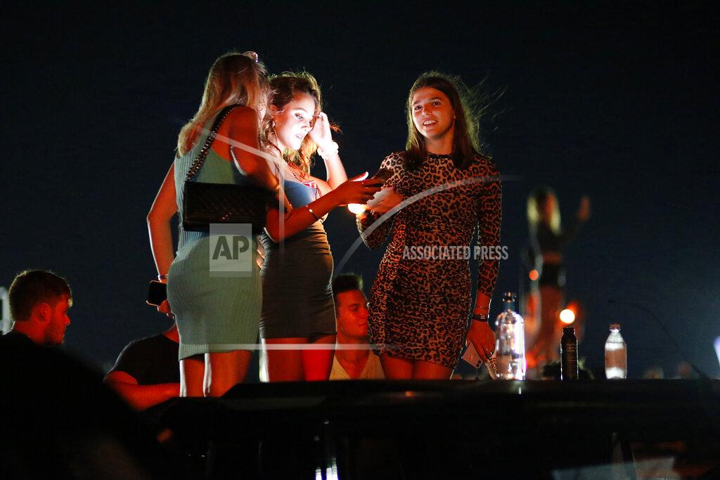 Rich Schineller In this July 25, 2020, photo provided by Rich Schineller, three young women emerge through the roof of an open vehicle and stand close to one another without wearing any face coverings at the "Safe & Sound" concert in Southampton, N.Y. New York Gov. Andrew Cuomo says he is "appalled" by videos showing crowds standing close together at a Hamptons concert featuring electronic music duo The Chainsmokers over the weekend. (Rich Schineller via AP)