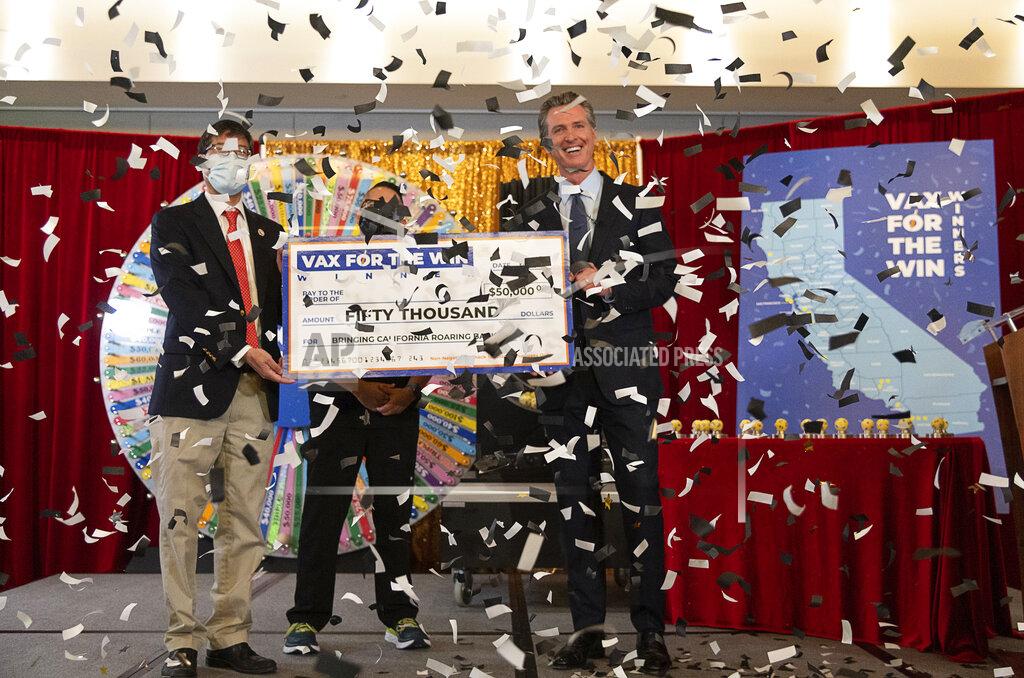 California Gov. Gavin Newsom, State Sen. Richard Pan, left, and UC Davis Assistant Nurse Manager Claudio Alvarado, center, hold a mock check as the state drew the first 15 winners to be awarded $50,000 for getting vaccinated against COVID-19, at the California Lottery Headquarters on Friday, June 4, 2021, in Sacramento, Calif. It was the first in a series of drawings for $16.5 million in prize money aimed at encouraging Californians to get their shots ahead of June 15, when the state plans to lift almost all virus-related restrictions. (Paul Kitagaki Jr./The Sacramento Bee via AP)