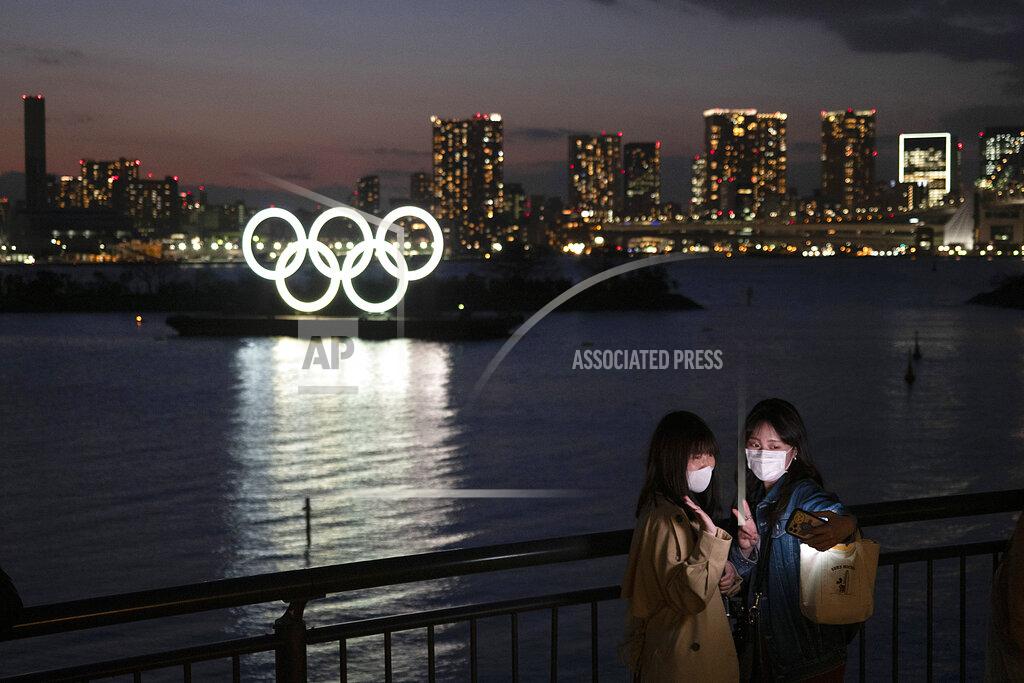 Two women take a selfie with the Olympic rings in the background in the Odaiba section of Tokyo, Thursday, March 12, 2020. Doping testers around the sporting world are trying to avoid infecting themselves or athletes during the global virus outbreak, and that's not easy when collecting samples means getting very close to sports stars. (AP Photo/Jae C. Hong)