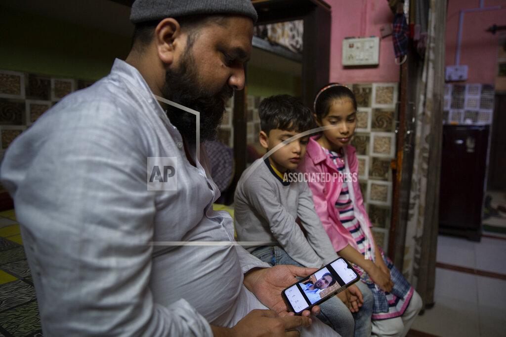 Altaf Qadri Haroon, holds a mobile phone as his nephew and niece look at the photograph of their father who was shot and killed by their Hindu neighbors during February 2020 communal riots, in North Ghonda, one of the worst riot affected neighborhood, in New Delhi, India, Friday, Feb. 19, 2021. As the first anniversary of bloody communal riots that convulsed the Indian capital approaches, Muslim victims are still shaken and struggling to make sense of their struggle to seek justice. (AP Photo/Altaf Qadri)