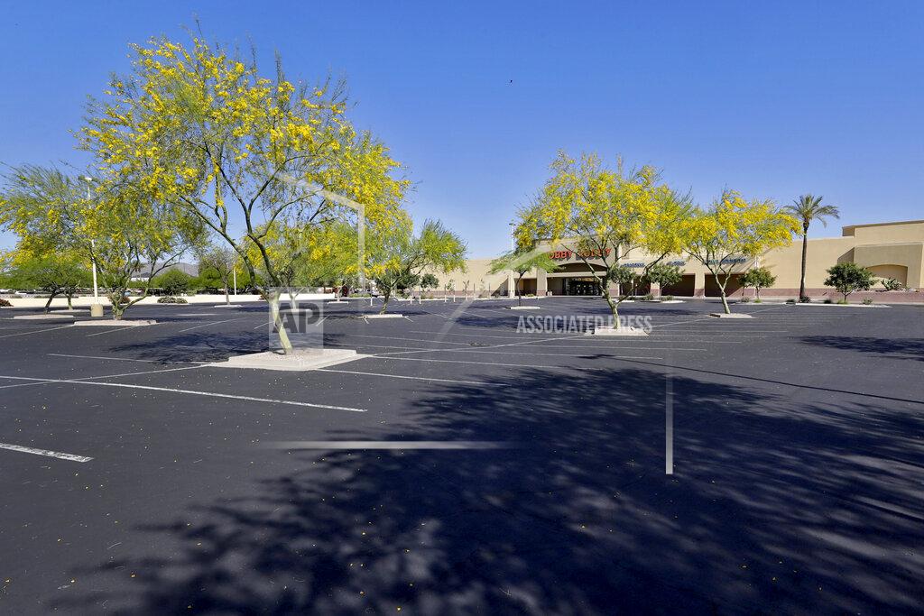 A parking lot outside closed businesses remains empty Friday, April 24, 2020, in Phoenix. The outbreak of the coronavirus has dealt a shock to the global economy with unprecedented speed and retail stores may have been changed forever by the outbreak. (AP Photo/Matt York)
