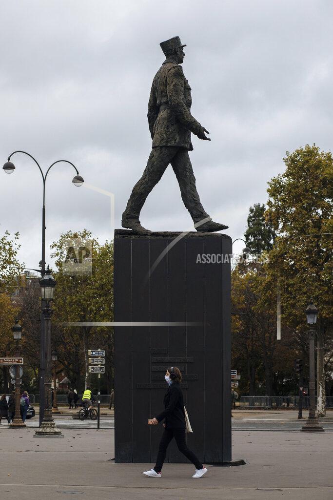 Lewis Joly A woman wearing a mask walks by a General de Gaulle statue, on the Champs Elysees avenue in Paris, Sunday Oct.25, 2020. A curfew intended to curb the spiraling spread of the coronavirus, has been imposed in many regions of France including Paris and its suburbs. (AP Photo/Lewis Joly)