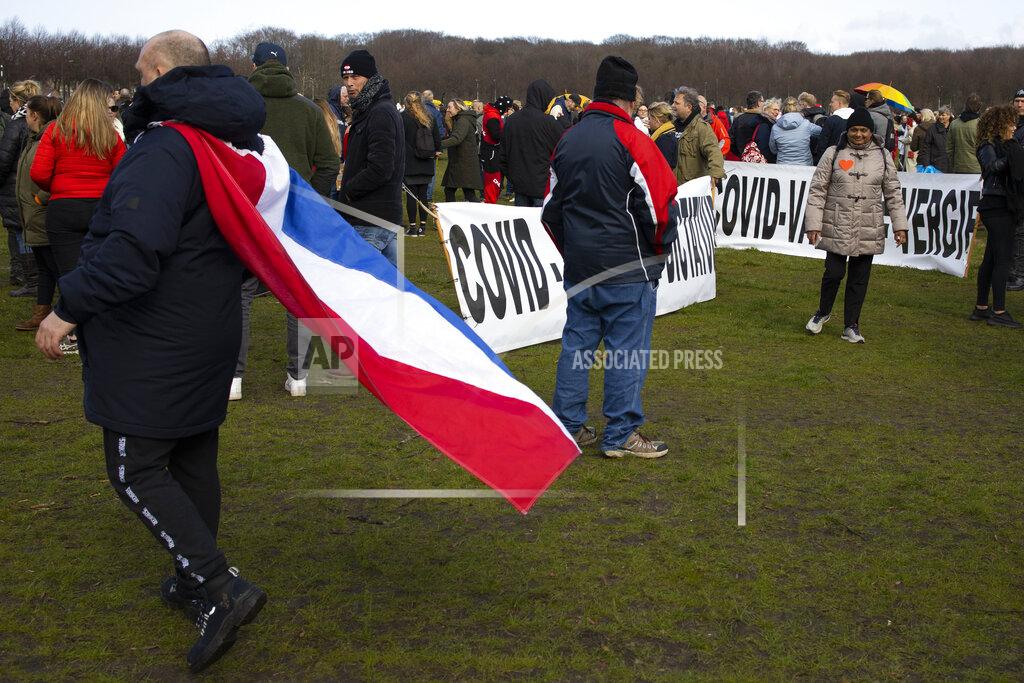 Peter Dejong A man wearing a Dutch flag passes signs reading "COVID Rules = Dictatorship" and "COVID Vaccin = Poison" during a demonstration ahead of three days of voting starting Monday in a general election, to protest government policies including the curfew, lockdown and coronavirus related restrictions in The Hague, Netherlands, Sunday, March 14, 2021. (AP Photo/Peter Dejong)