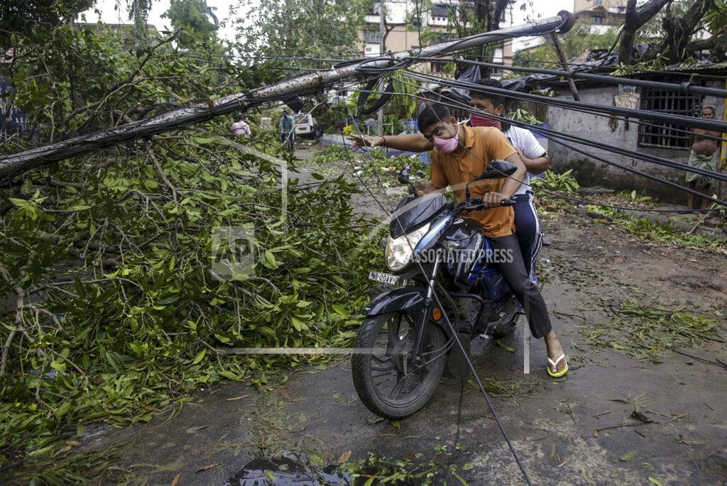 Bikas Das People make their way through damaged cables and a tree branch fallen in the middle of a road after Cyclone Amphan hit the region in Kolkata, India, Thursday, May 21, 2020. A powerful cyclone ripped through densely populated coastal India and Bangladesh, blowing off roofs and whipping up waves that swallowed embankments and bridges and left entire villages without access to fresh water, electricity and communications. (AP Photo/Bikas Das)