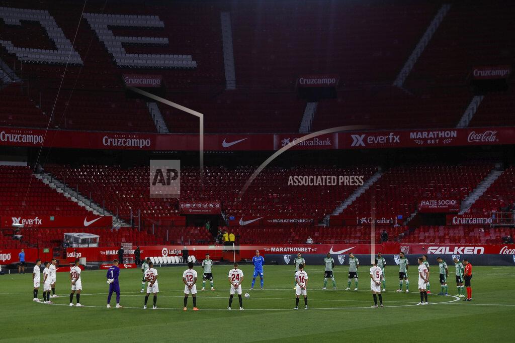 Str Sevilla and Betis players stand during a minute of silence before the start of their Spanish La Liga soccer match in Seville, Spain, Thursday, June 11, 2020. With virtual crowds, daily matches and lots of testing for the coronavirus, soccer is coming back to Spain. The Spanish league resumes this week more than three months after it was suspended because of the pandemic, becoming the second top league to restart in Europe. The Bundesliga was first. The Premier League and the Italian league should be next in the coming weeks. (AP Photo)