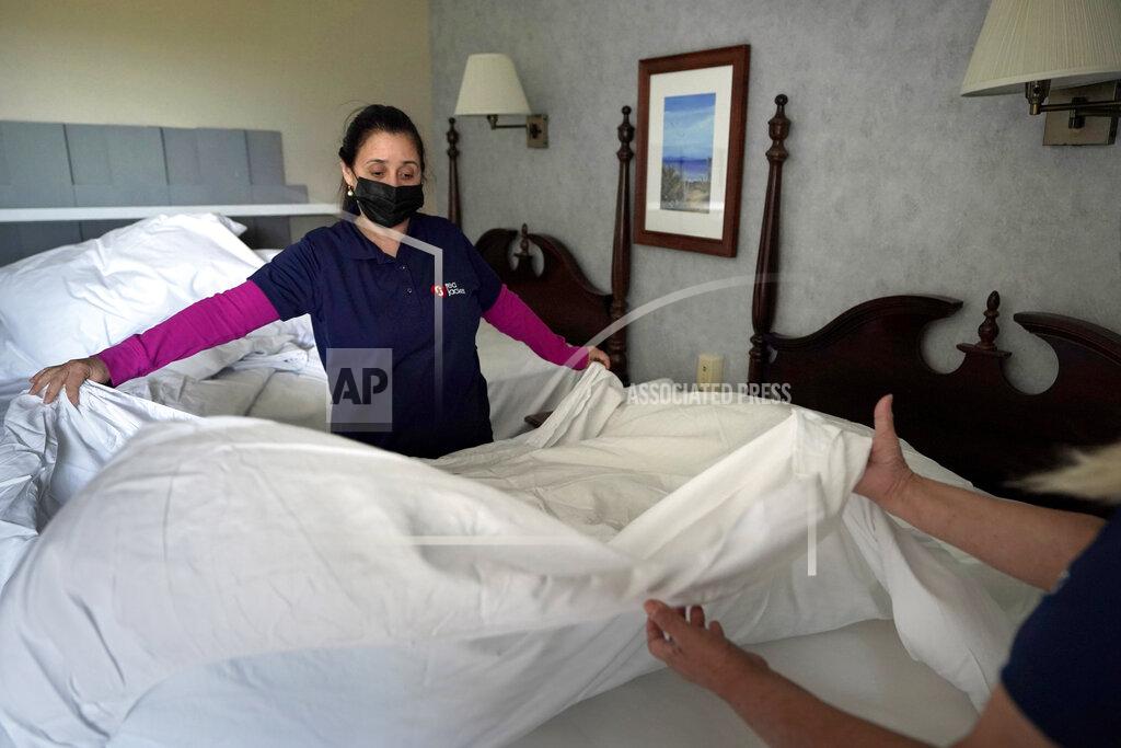 Steven Senne Workers Miriam Mattos, left, and Marilene Souto, hands only at right, both of Hyannis, Mass., make a bed, Tuesday, April 6, 2021, at Red Jacket Resorts, in Yarmouth, Mass. Hotels, restaurants and other businesses in tourist destinations are warning that hiring challenges during the coronavirus pandemic could force them to pare back operating hours or curtail services just as they’re eyeing a bounce-back summer. (AP Photo/Steven Senne)