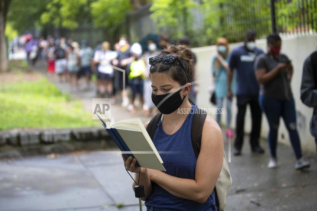 John Bazemore Kelsey Luker reads as she waits in line to vote, Tuesday, June 9, 2020, in Atlanta. Luker said she had been in line for almost two hours. Voters reported wait times of three hours. (AP Photo/John Bazemore)