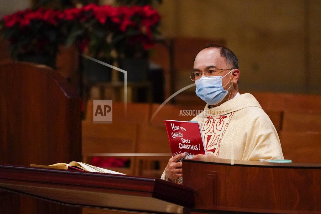 Ashley Landis Father David Gallardo holds up a copy of Dr. Seuss' "How the Grinch Stole Christmas" and likens the Grinch to COVID-10 during a Christmas Eve Mass at Cathedral of Our Lady of the Angels Thursday, Dec 24, 2020, in Los Angeles. California became the first state to record 2 million confirmed coronavirus cases, reaching the milestone on Christmas Eve as nearly the entire state was under a strict stay-at-home order and hospitals were flooded with the largest crush of cases since the pandemic began. (AP Photo/Ashley Landis)