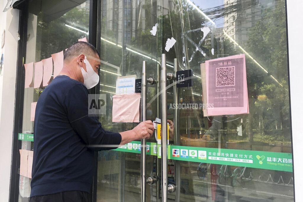 Chen Si A man tries to receive medicine he bought at a pharmacy through its closed glass doors in Shanghai, China, Sunday, May 22, 2022. Numerous residential compounds in Beijing have restricted movement in and out, although conditions remain far less severe than in Shanghai, where millions of citizens have been under varying degrees of lockdown for two months. (AP Photo/Chen Si)