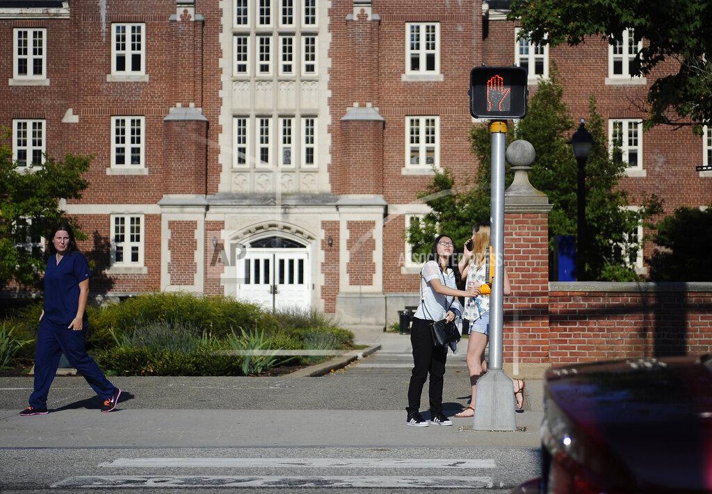 FILE- In this Sept. 18, 2015 file photo, a University of Connecticut student pushes a button at a crosswalk outside one of the student dormitories, in Storrs, Conn. On Friday, Oct. 30, 2020, the university ordered residential students in Storrs to stay away from all off-campus social gatherings until the middle of next week amid a spike in COVID-19 cases. (AP Photo/Jessica Hill, File)