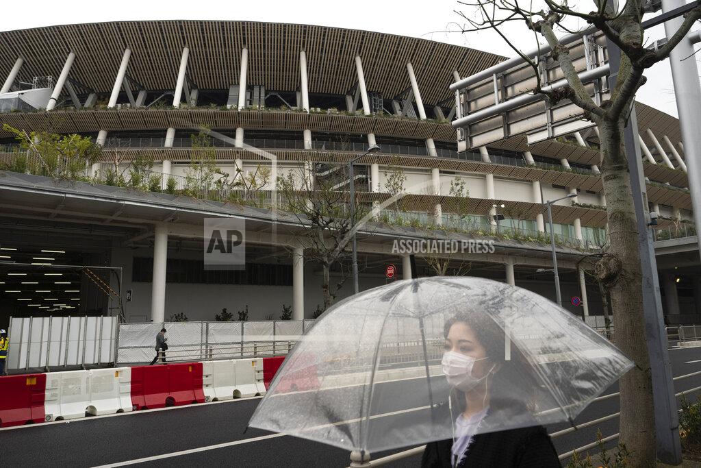 A woman walks past the New National Stadium, a venue for the opening and closing ceremonies at the Tokyo 2020 Olympics, in Tokyo, Monday, March 23, 2020. The IOC will take up to four weeks to consider postponing the Tokyo Olympics amid mounting criticism of its handling of the coronavirus crisis that now includes a call for delay from the leader of track and field, the biggest sport at the games. (AP Photo/Jae C. Hong)
