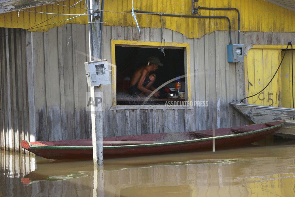 Edmar Barros A resident crouches on a raised floor set up inside a home to stay above floodwaters in Anama, Amazonas state, Brazil, Thursday, May 13, 2021. (AP Photo/Edmar Barros)