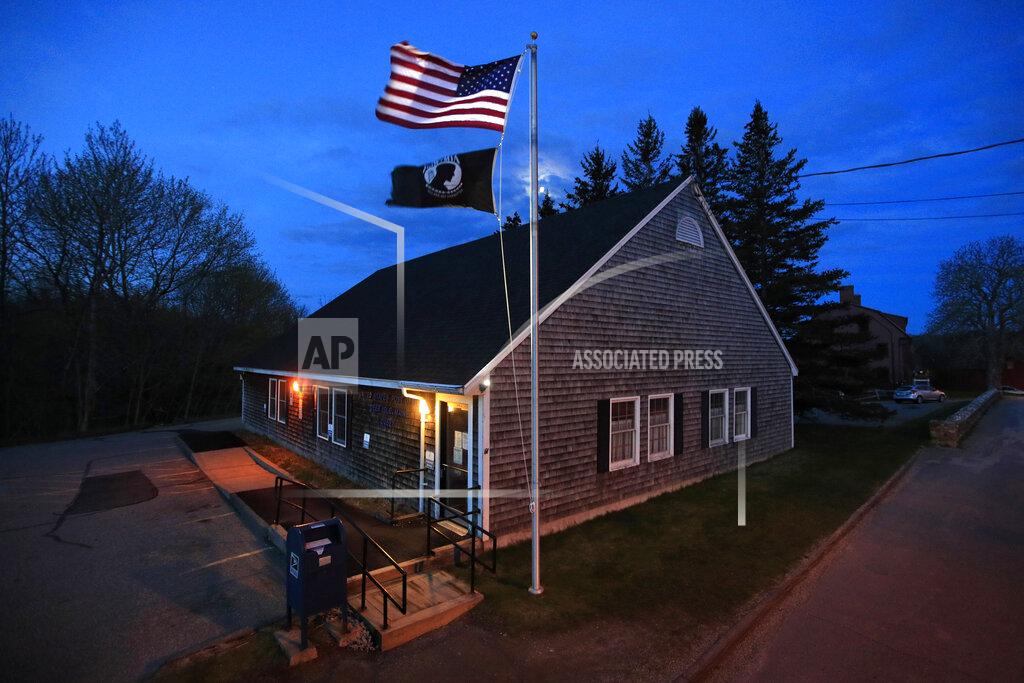In this Sunday, May 10, 2020, photo a new American flag flies outside the post office on Deer Isle, Maine. The flag was secretly replaced after a plea was posted on the post office bulletin board for help removing the old tattered flag that had been stuck on the pole. "It was really important that the flag be replaced, as a symbol of hope for all of us that there is a new day coming," said community health director Rene Colson Hudson. (AP Photo/Robert F. Bukaty)