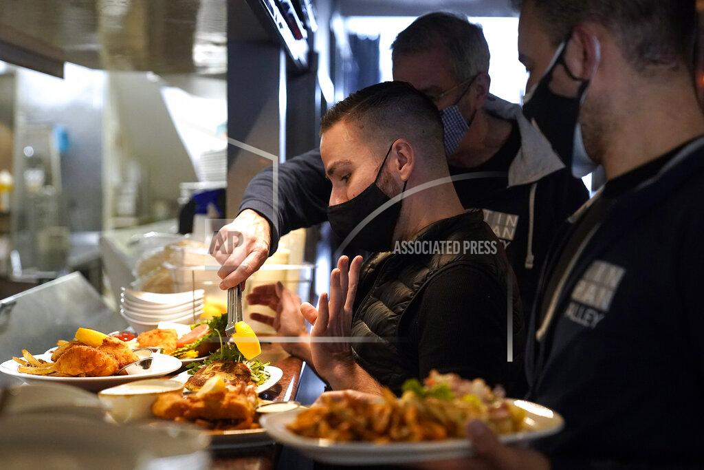 Steven Senne Server Christopher Lee-Caron, of Provincetown, Mass., center left, prepares to carry plates of food to customers at Tin Pan Alley restaurant, Tuesday, April 6, 2021, in Provincetown. Hotels, restaurants and other businesses in tourist destinations are warning that hiring challenges during the coronavirus pandemic could force them to pare back operating hours or curtail services just as they’re eyeing a bounce-back summer. (AP Photo/Steven Senne)
