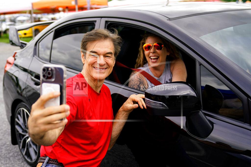 Matt Rourke Mehmet Oz, a Republican candidate for U.S. Senate in Pennsylvania, poses for a photograph with an attendee during his visit to a car show in Carlisle, Pa., Saturday, May 14, 2022. (AP Photo/Matt Rourke)