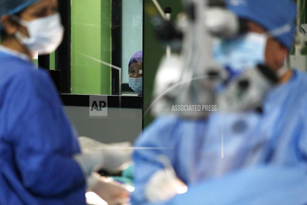 Niranjan Shrestha A Nepalese patient, center watches Dr. Sanduk Ruit perform cataract surgery as she waits her turn at the Tilganga Eye Center in Kathmandu, Nepal, March 26, 2021. Nepal’s “God of Sight” eye doctor renowned for his innovative and inexpensive cataract surgery for the poor is taking his work beyond the Himalayan mountains to other parts of the world so there is no more unnecessary blindness in the world. Ruit, who has won many awards for his work and performed some 130,000 cataract surgery in the past three decades, is aiming to expand his work beyond the borders of his home country and the region to go globally. (AP Photo/Niranjan Shrestha)