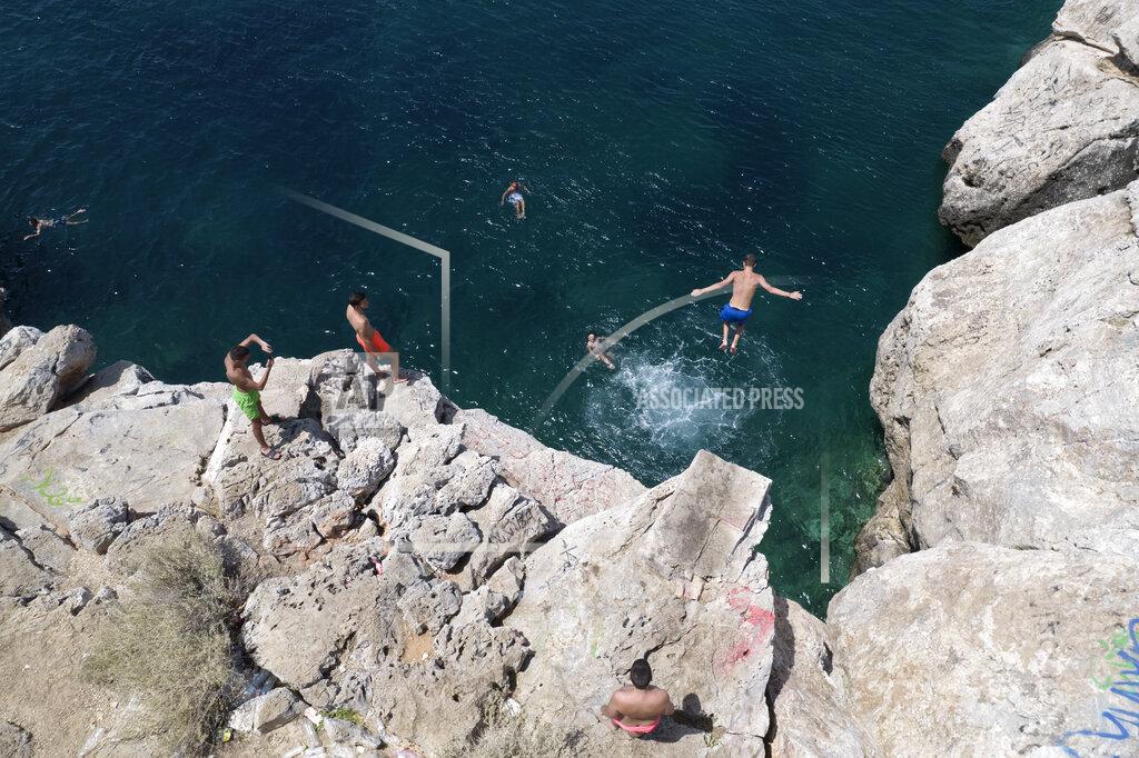 Yorgos Karahalis A youth jumps in the sea from a rock at Varkiza village, a few miles southwest of Athens, on Thursday, July 29, 2021. One of the most severe heat waves recorded since 1980s scorched southeast Europe on Thursday, sending residents flocking to the coast, public fountains and air-conditioned locations to find some relief, with temperatures rose above 40 C (104 F) in parts of Greece and across much of the region. (AP Photo/Yorgos Karahalis)