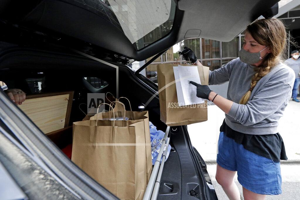 Nam Y. Huh Marry Hammell, a staffer from Alinea restaurant, places carryout orders in the trunk of a car for a customer in Chicago, Saturday, June 20, 2020. Due to the coronavirus Alinea shifted to carryout on March 17. Since then, it has served 82,000 meals, said Nick Kokonas, the restaurant's co-owner. (AP Photo/Nam Y. Huh)