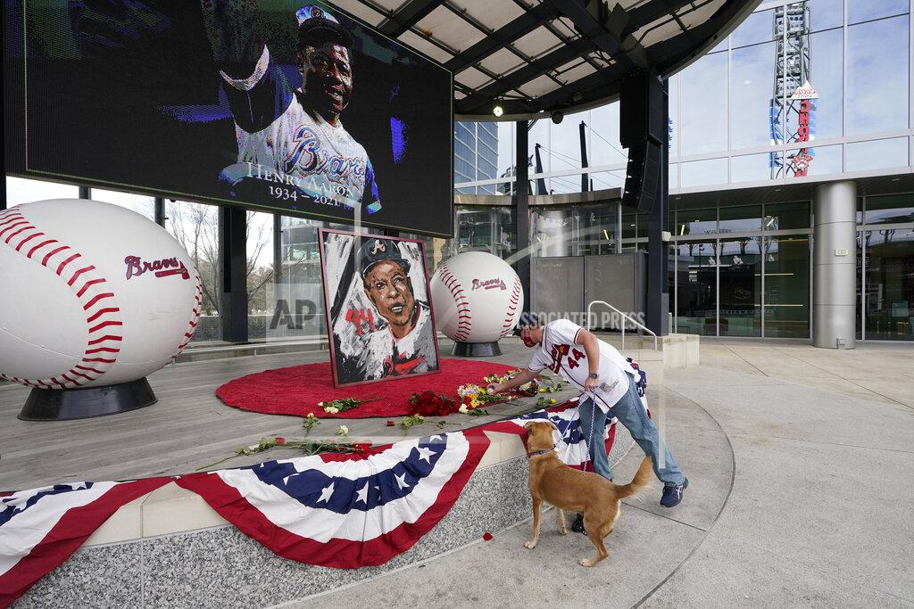 John Bazemore A man places flowers next to a portrait Atlanta Braves' Hank Aaron outside Truist Park, Friday, Jan. 22, 2021, in Atlanta. Aaron, who endured racist threats with stoic dignity during his pursuit of Babe Ruth but went on to break the career home run record in the pre-steroids era, died peacefully in his sleep early Friday. He was 86. (AP Photo/John Bazemore