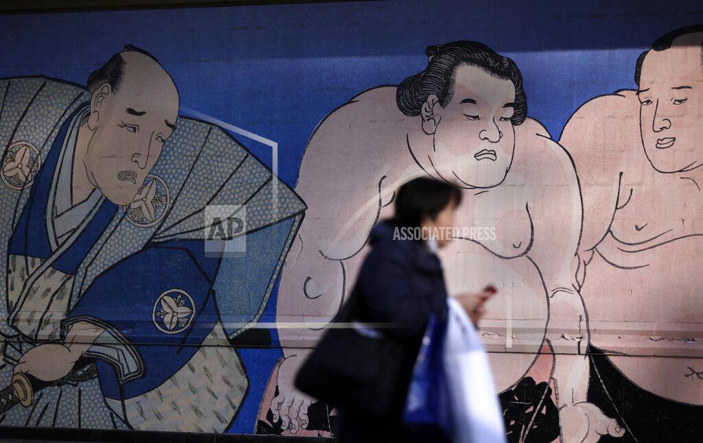 FILE - In this Nov. 18, 2016, file photo, a woman walks past a sumo mural at the Ryogoku Kokugikan, Japan's national sumo stadium, in Tokyo. A Japanese sumo wrestler died of acute respiratory failure Wednesday, April 28, 2021, after suffering a head injury during his bout in a tournament last month, in a case that brought sumo’s emergency response into question. (AP Photo/Eugene Hoshiko, File)