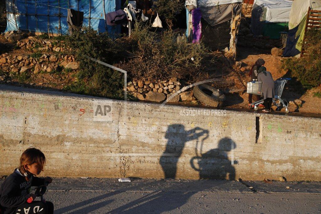Thanassis Stavrakis Children play as others put water on a shopping cart outside the perimeter of the overcrowded refugee camp at the port of Vathy on the eastern Aegean island of Samos, Greece, Tuesday, Feb. 23, 2021. On a hill above a small island village, the sparkling blue of the Aegean just visible through the pine trees, lies a boy’s grave. His first ever boat ride was to be his last - the sea claimed him before his sixth birthday. His 25-year-old father, like so many before him, had hoped for a better life in Europe, far from the violence of his native Afghanistan. But his dreams were dashed on the rocks of Samos, a picturesque Greek island almost touching the Turkish coast. Still devastated from losing his only child, the father has now found himself charged with a felony count of child endangerment. (AP Photo/Thanassis Stavrakis)